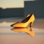 A pair of yellow high-heeled shoes, embodying key trends, is placed side by side on a reflective surface, casting clear reflections. The background is blurred, with soft lighting suggesting a sunset or sunrise ambiance.